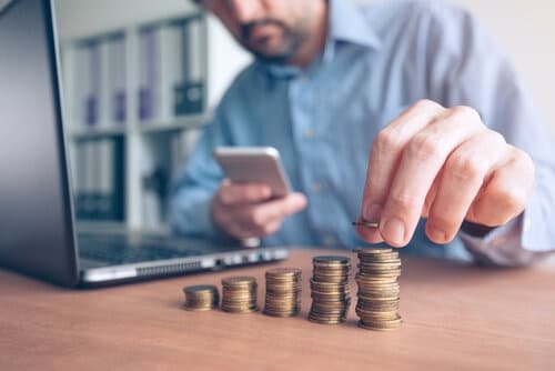 finances-and-budgeting-businessman-stacking-coins-GYFTLC6 (1) business man budgeting, stacking coins on the desk, looking at calculator